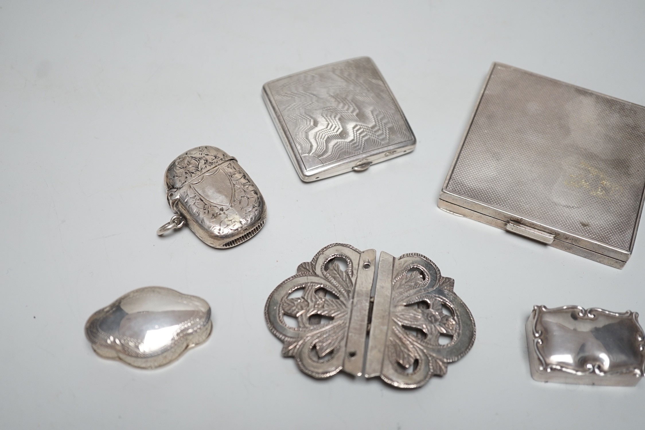 A George VI engine turned silver compact, 69mm, two modern silver pill boxes, a Persian white metal belt buckle, a silver vesta case and a base metal compact.